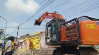 Petugas saat menurunkan alat berat untuk membongkar bangunan permanen.