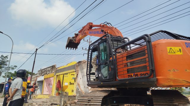 Petugas saat menurunkan alat berat untuk membongkar bangunan permanen.